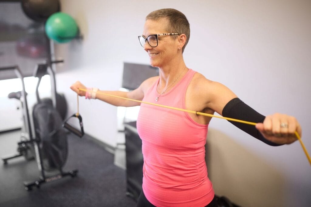 Breast cancer survivor wearing pink exercises with a resistance band at AIM Fitness & Nutrition in Gretna during Project Pink’d partnership session.